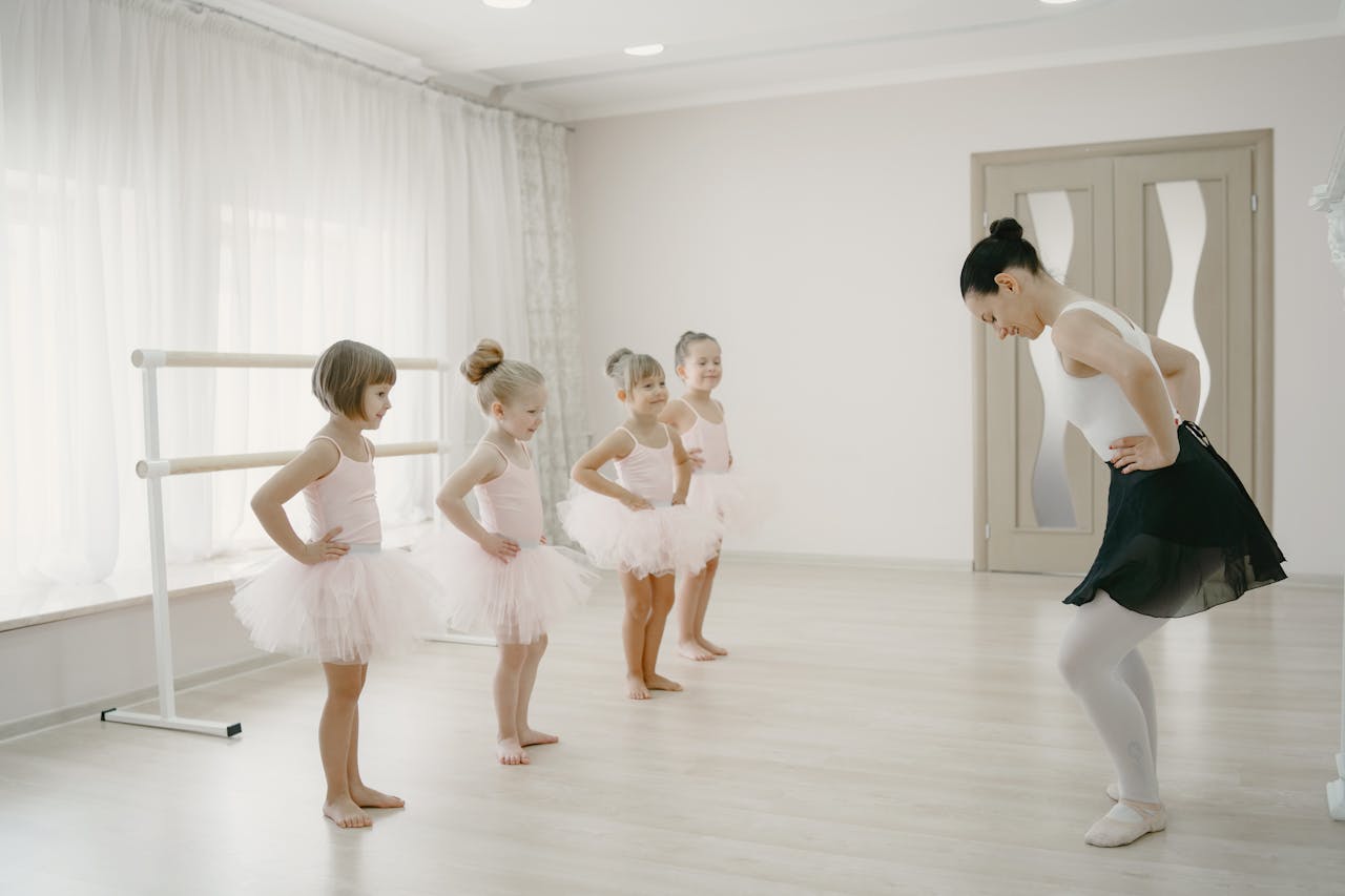 A group of young ballerinas learning ballet with their instructor in a bright studio.